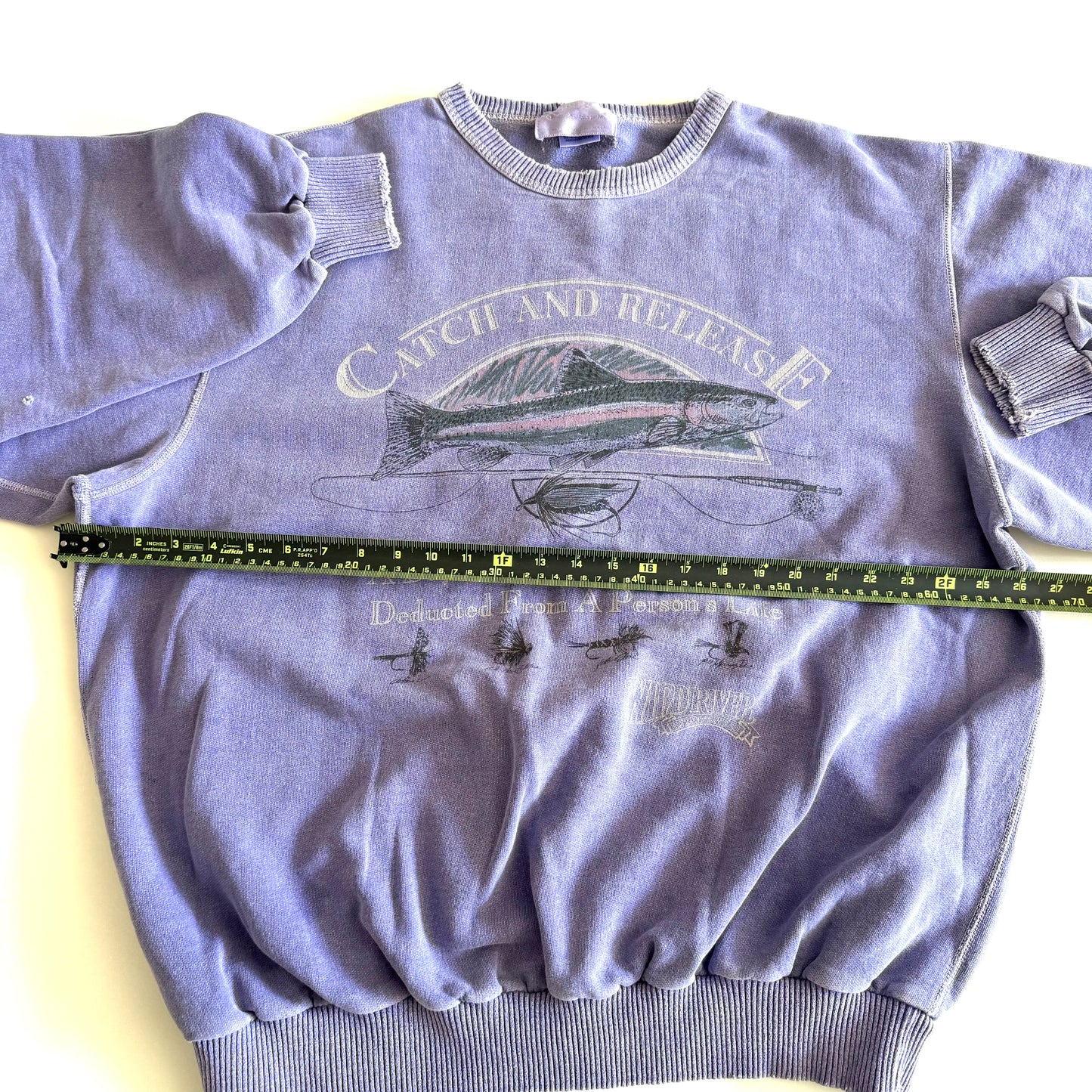 Light purple sweatshirt with fishing theme images and words on the front, on a white backdrop - with a measuring tape laid on it.