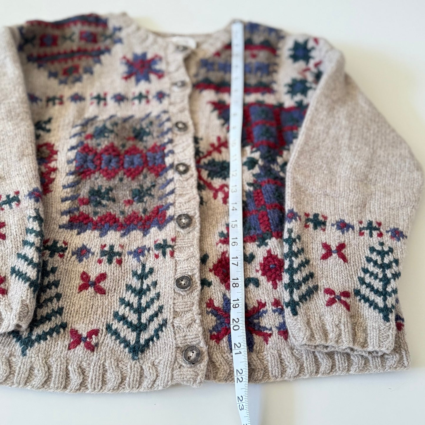Knitted cardigan with a patterned design and a measuring tape laid over it on a white background
