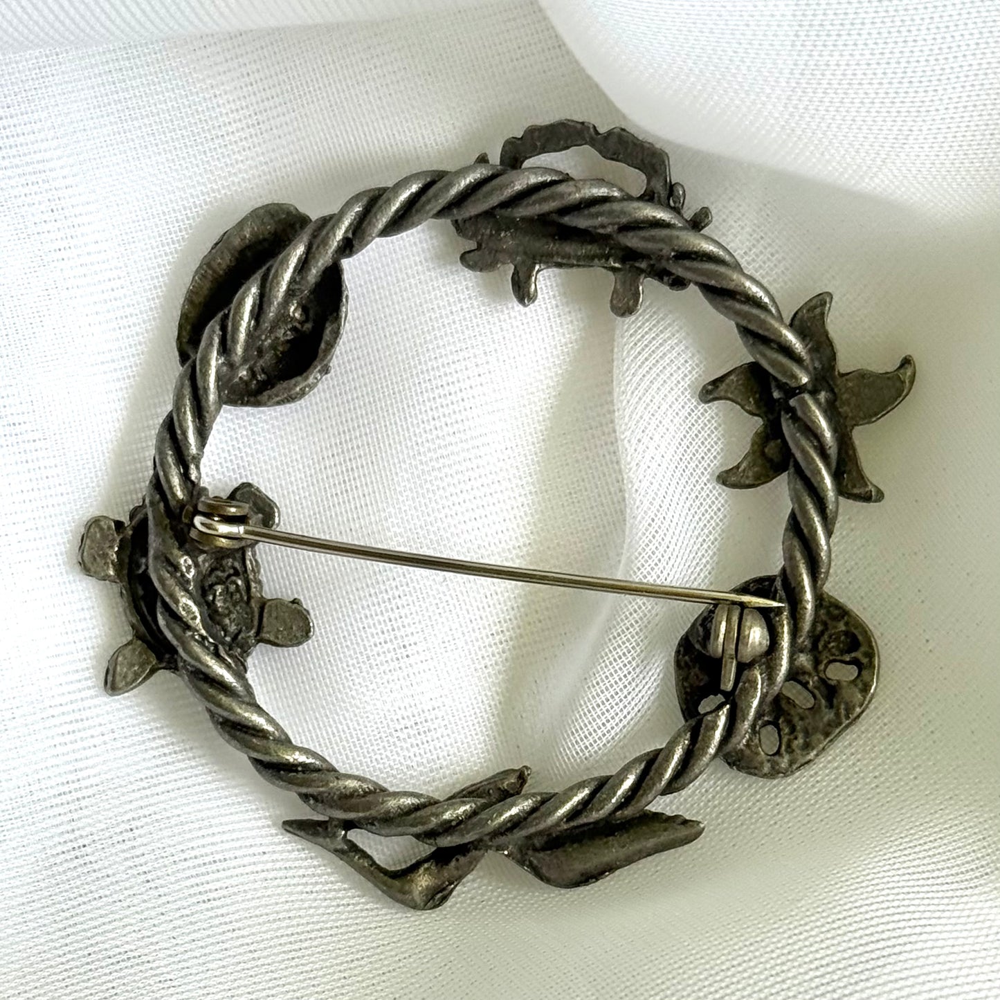 Silver brooch with twisted design on a white fabric background
