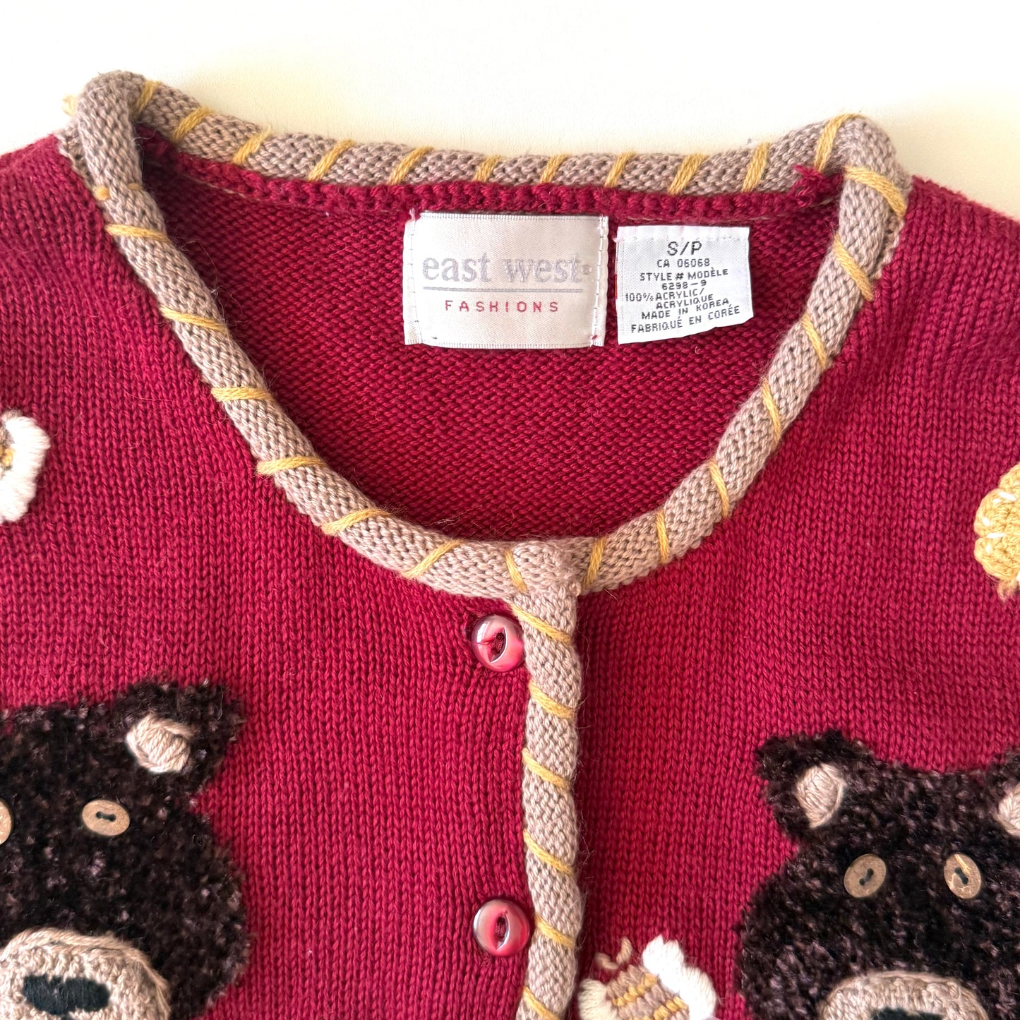 Close-up of a red cardigan with bear designs and 'east west fashions' label.