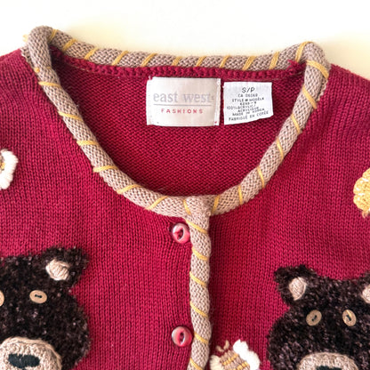 Close-up of a red cardigan with bear designs and 'east west fashions' label.