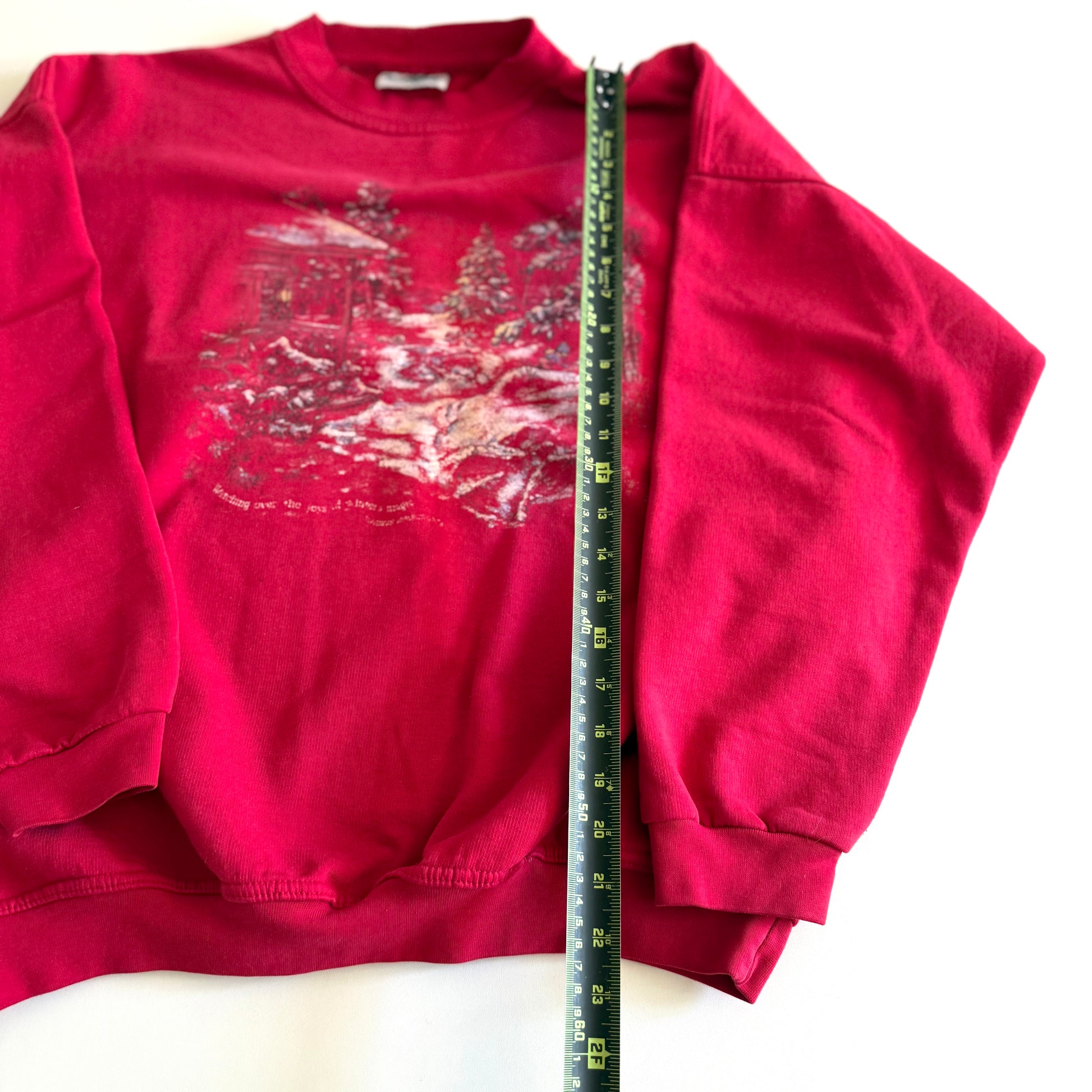 Bold pink sweatshirt / crewneck with a winter scene on the front  laid on a white backdrop - with a measuring tape laid out on it. 