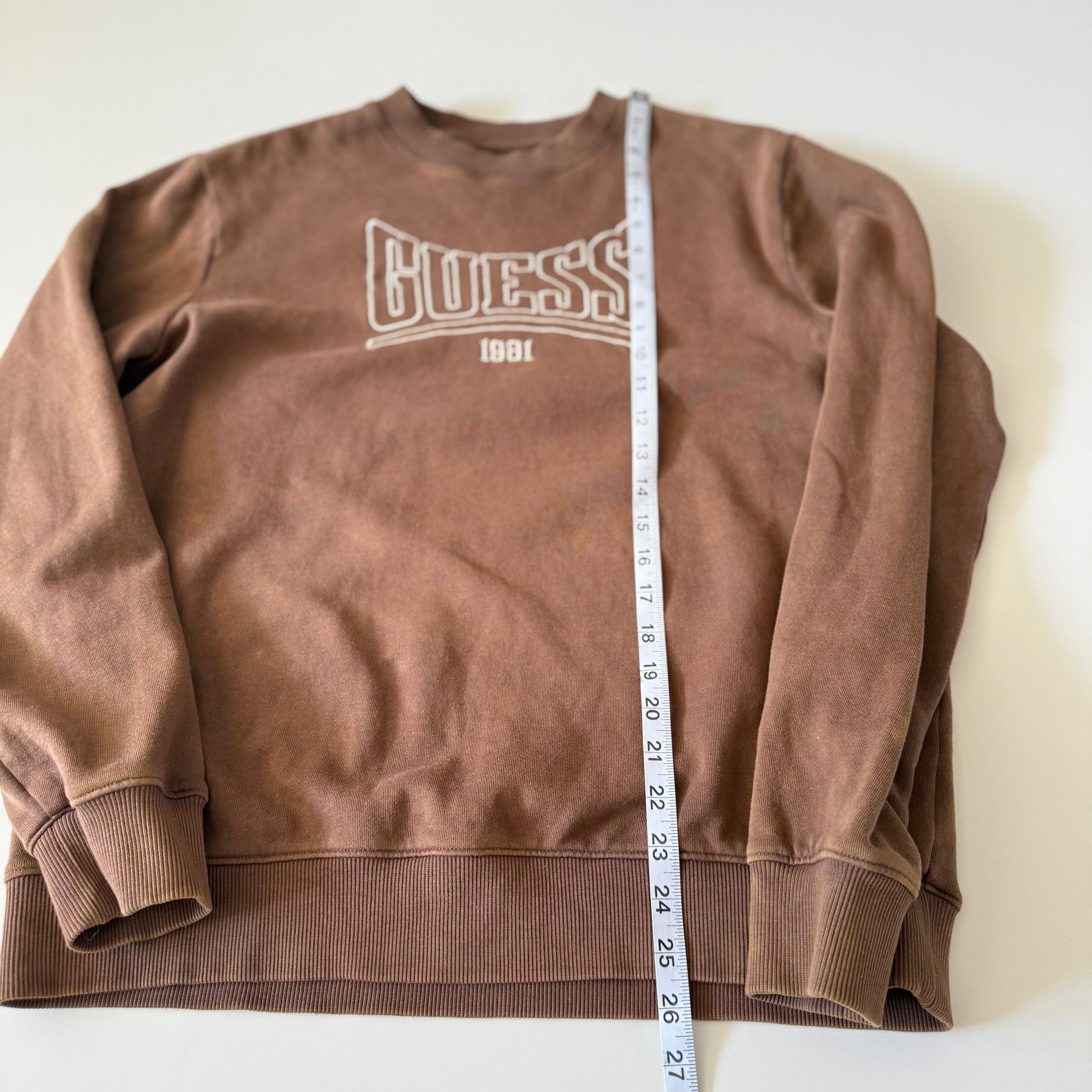 Brown sweatshirt with 'Guess' logo and a measuring tape on a white background