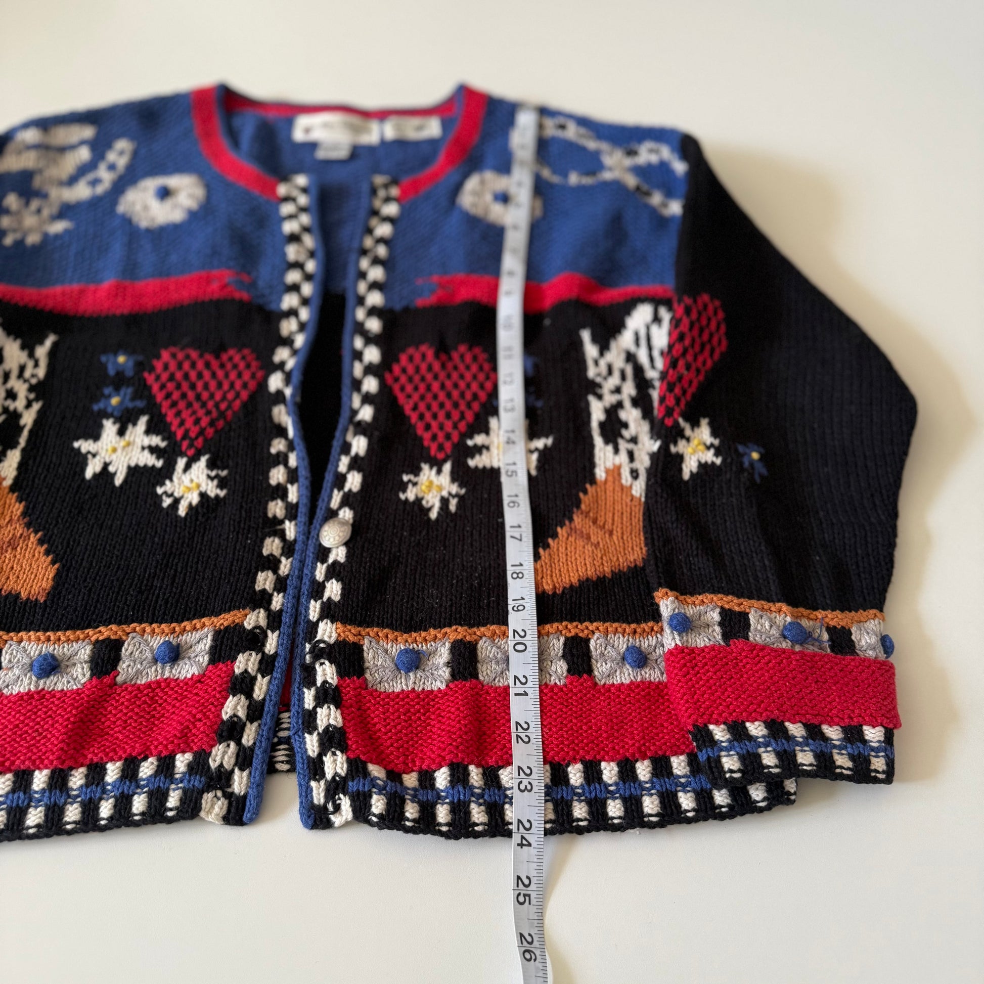 Colorful knitted cardigan with heart patterns and a measuring tape for size reference on a white background