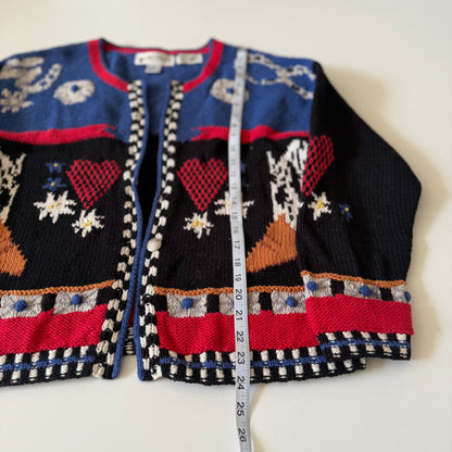 Colorful knitted cardigan with heart patterns and a measuring tape for size reference on a white background