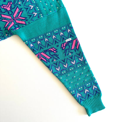 Just a photo of the arm of the Teal and pink sweater with an aztec / snowflake adjacent style pattern, on a white background. 