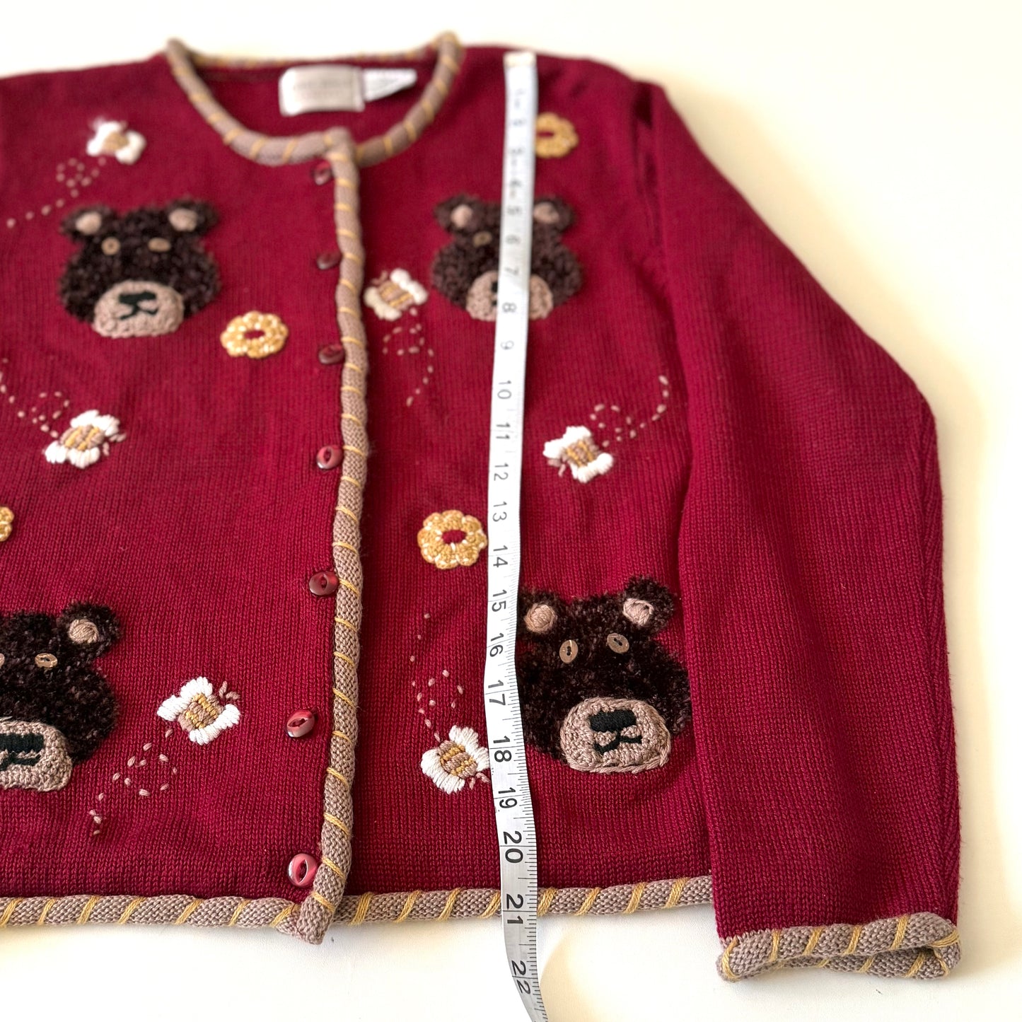 Red sweater with bear designs and a measuring tape for size reference on a white background