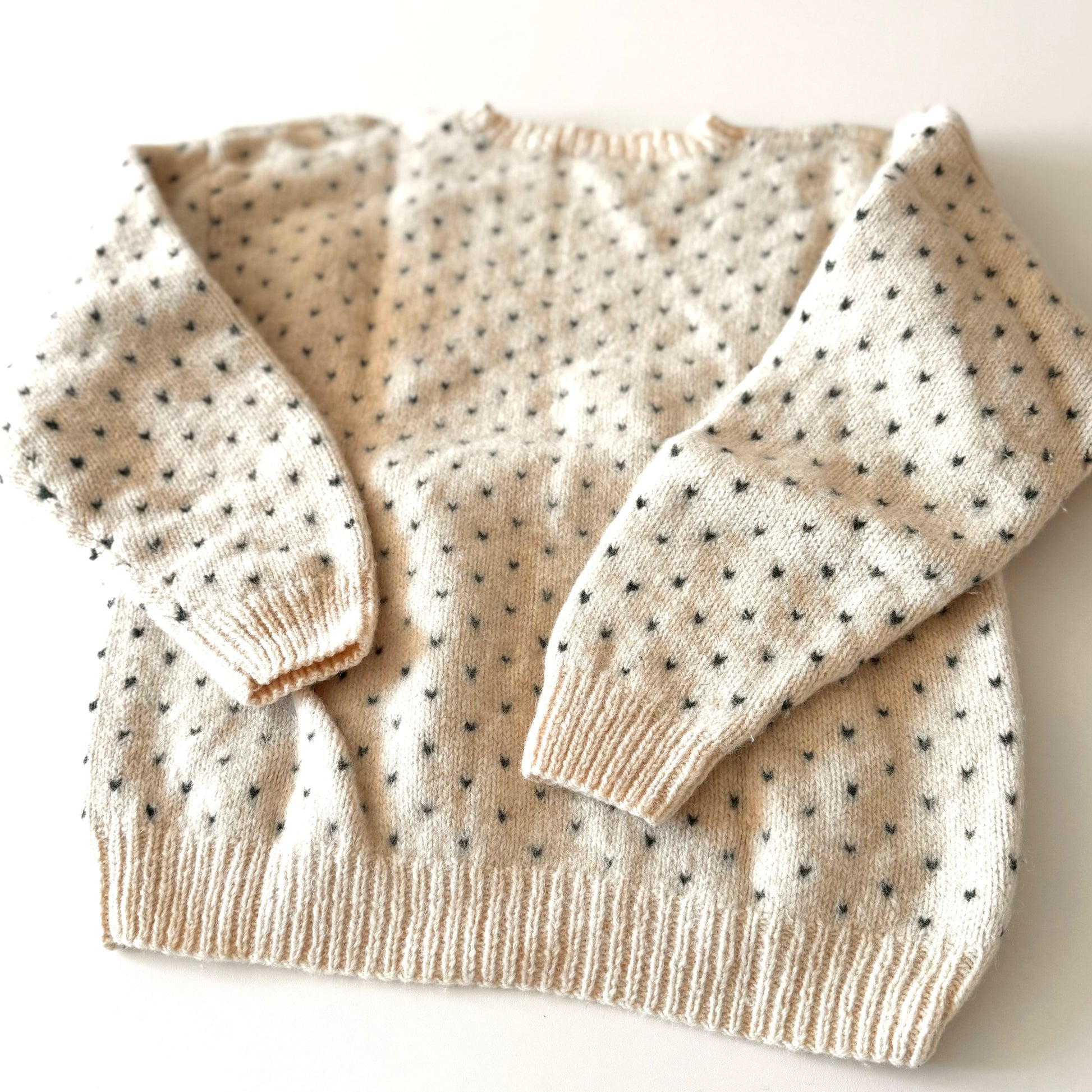 Beige sweater with black dot pattern on a white background
