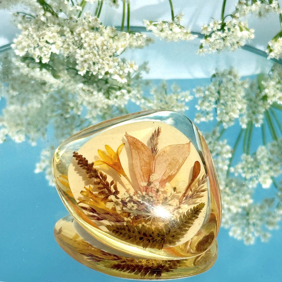 Gold teardrop-shaped jewelry piece with a blue background and white flowers
