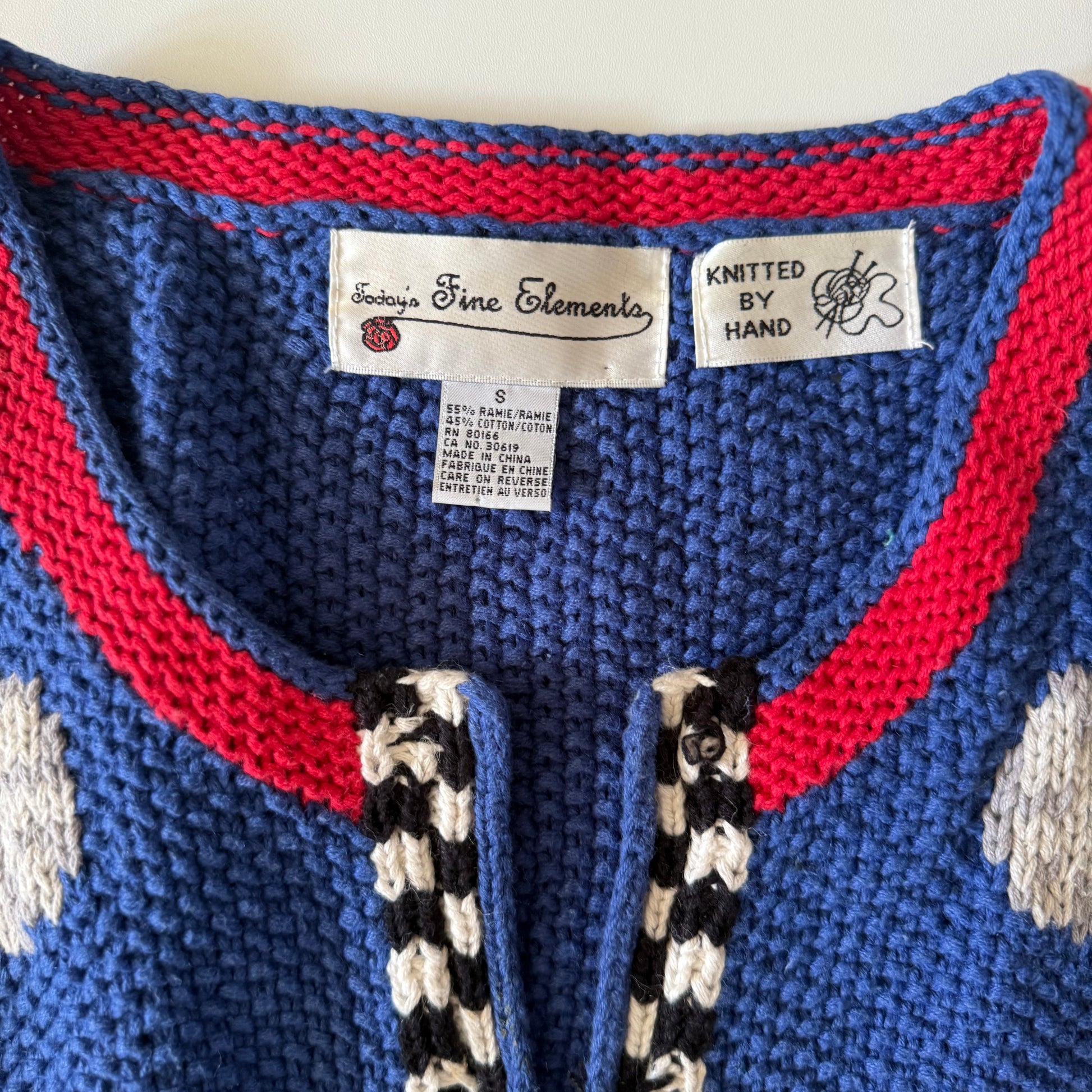 Close-up of a blue knitted garment with red trim and brand labels.