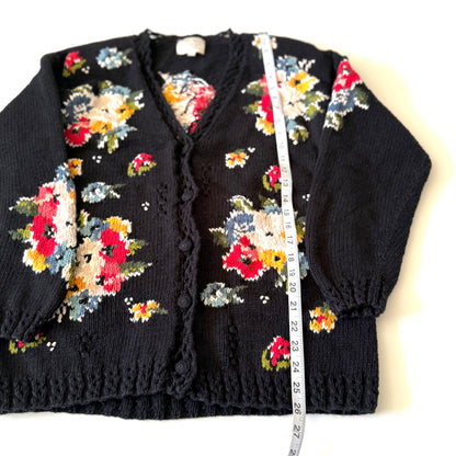 Black cardigan with colorful floral patterns and a measuring tape on a white background
