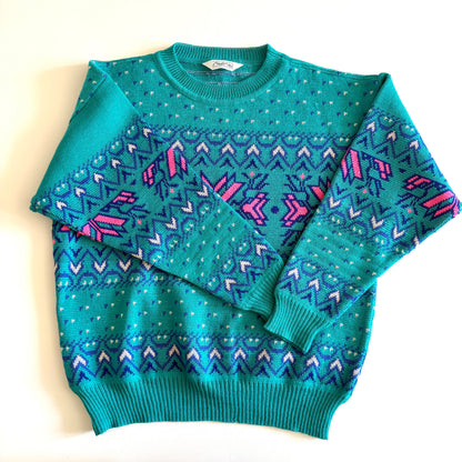 Teal and pink sweater with an aztec / snowflake adjacent style pattern, on a white background. 