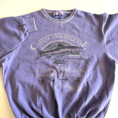Light purple sweatshirt with fishing theme images and words on the front, on a white backdrop. 