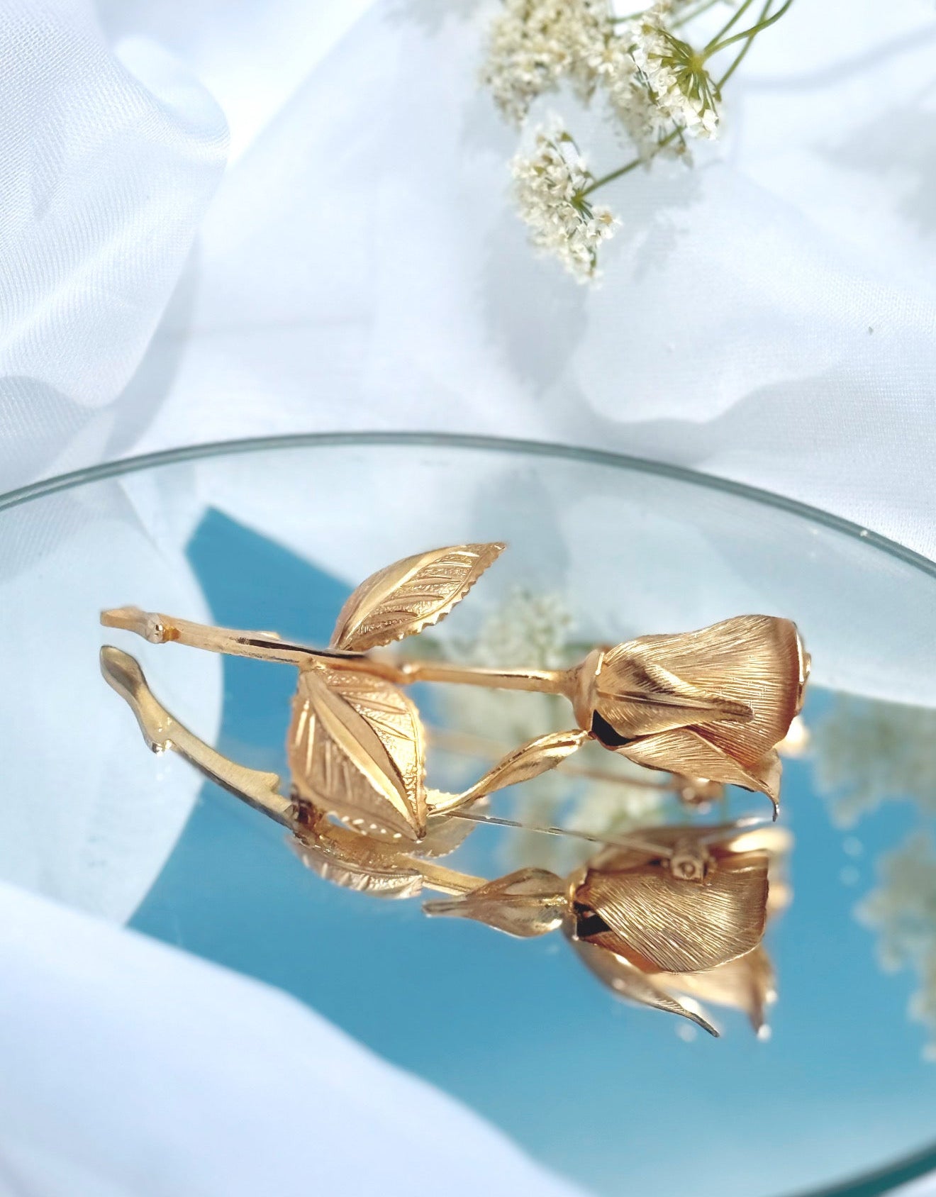 Gold rose-shaped brooch on a reflective surface with a light background