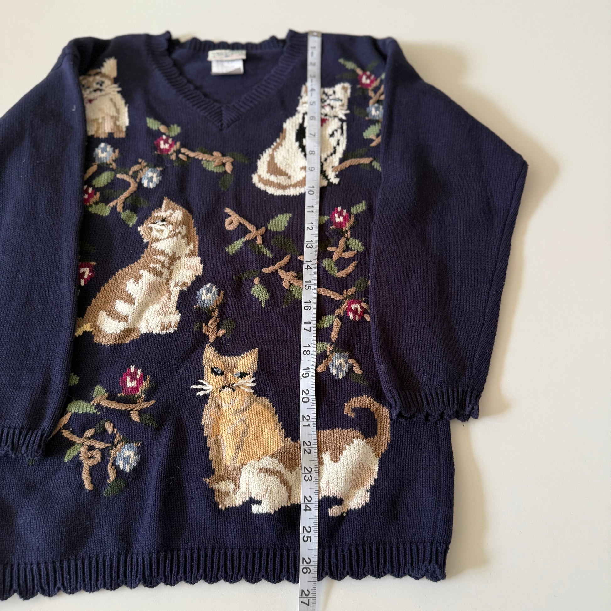 Navy blue sweater with cat pattern and measurement tape on a white background
