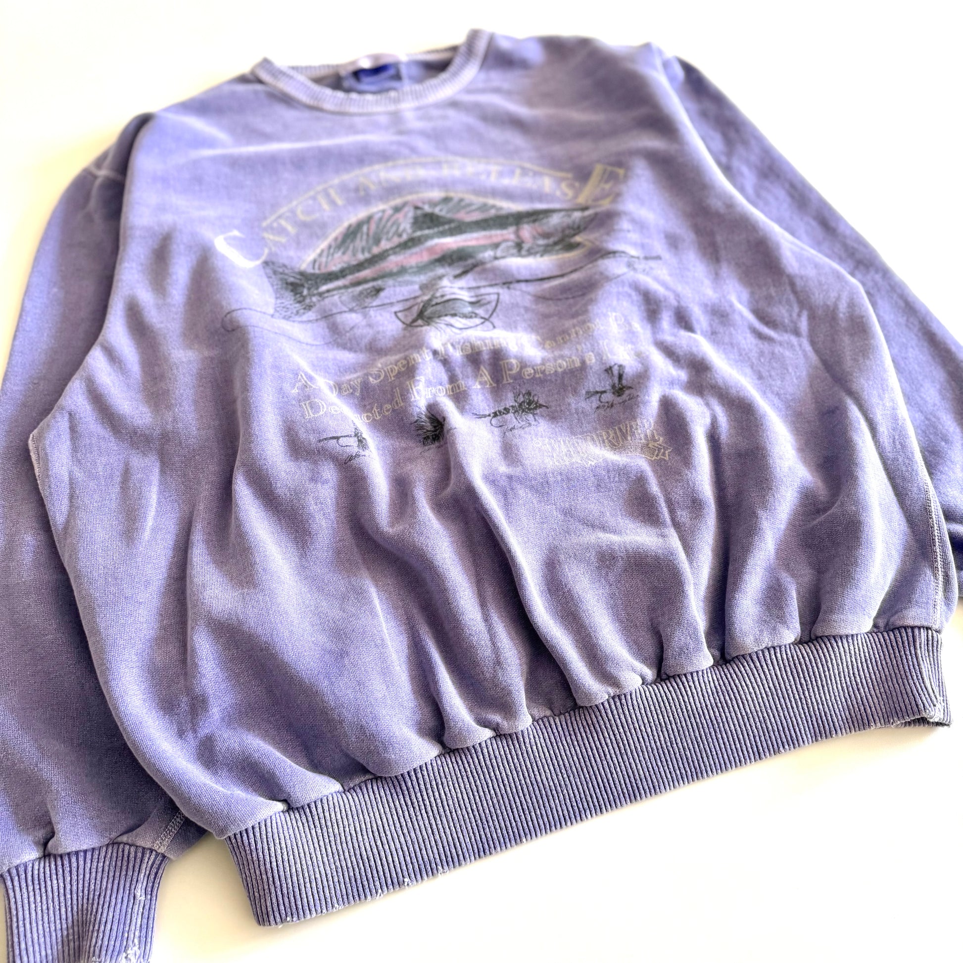 Light purple sweatshirt with fishing theme images and words on the front, on a white backdrop. 