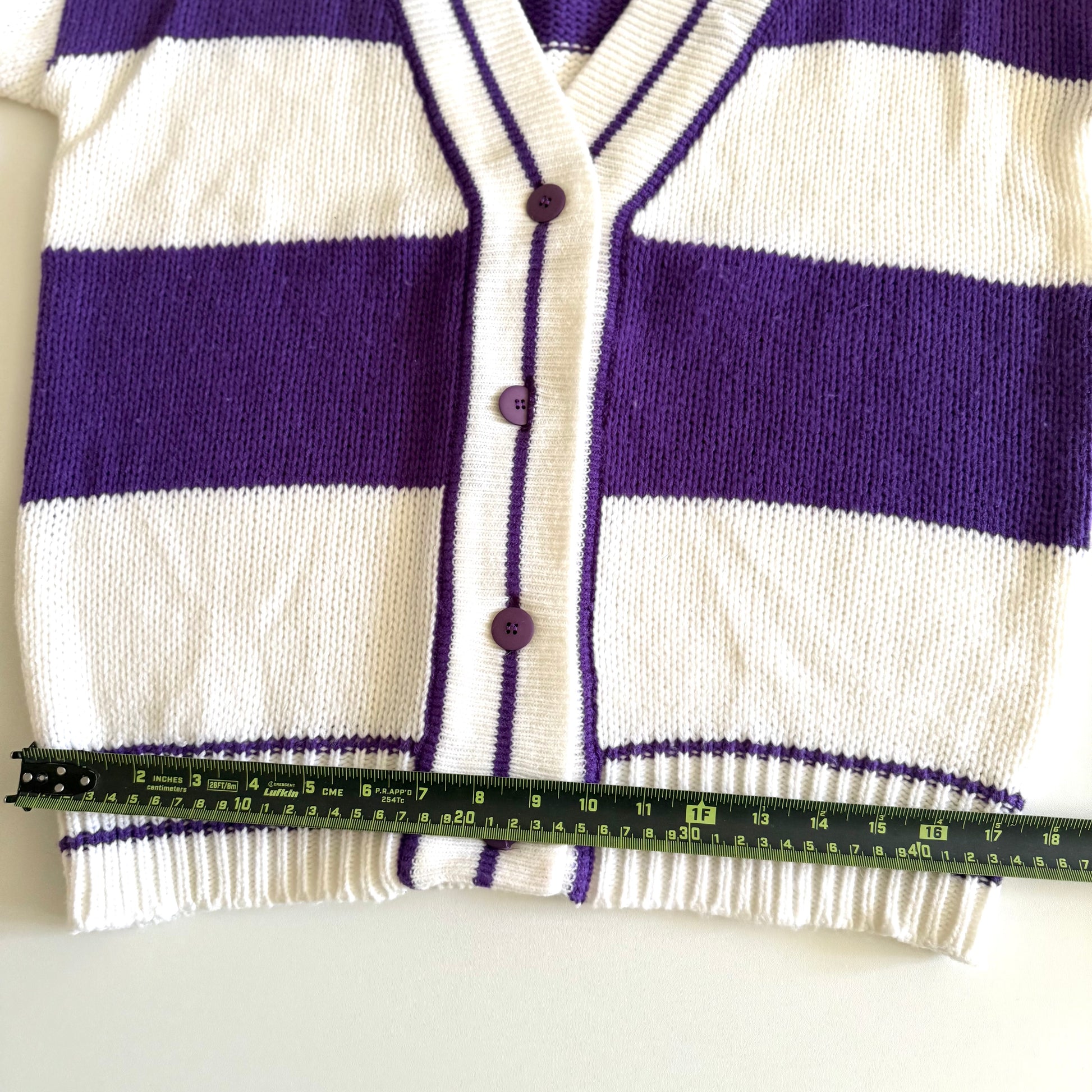 1990's preppy style - purple and white striped cardigan with a measuring tape on it on a white backdrop. 