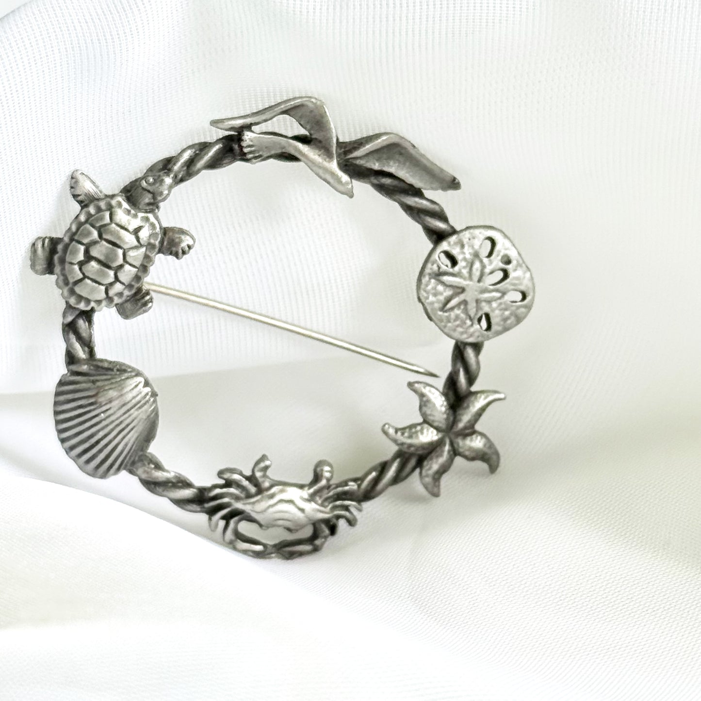 Silver brooch with turtle, shell, and starfish design on a white background