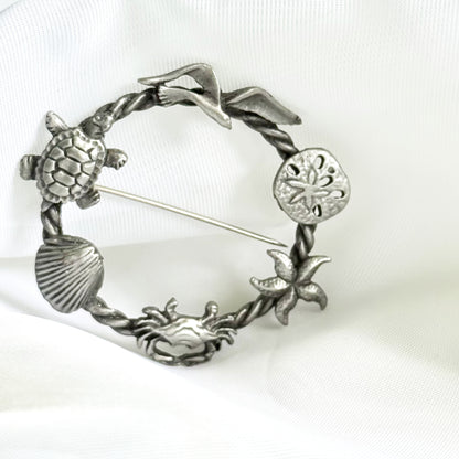 Silver brooch with turtle, shell, and starfish design on a white background