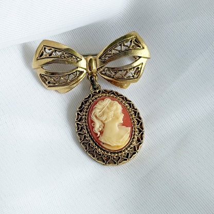 Gold bow-shaped brooch with a cameo pendant on a white background