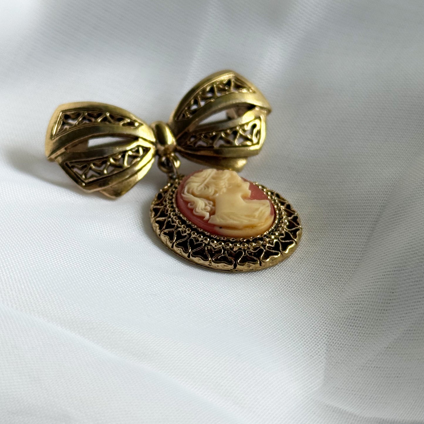 Gold bow-shaped brooch with a cameo pendant on a white fabric background