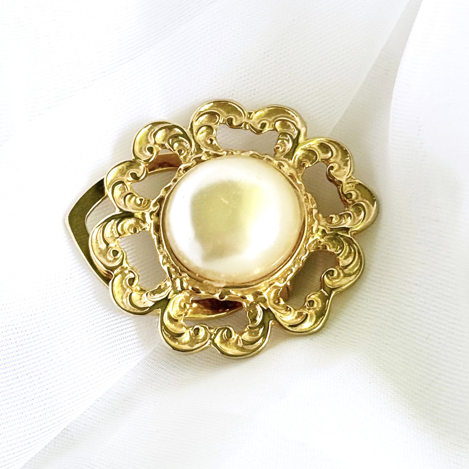 Decorative brooch with gold frame and pearl center on a white background