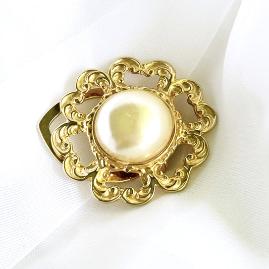 Decorative brooch with gold frame and pearl center on a white background