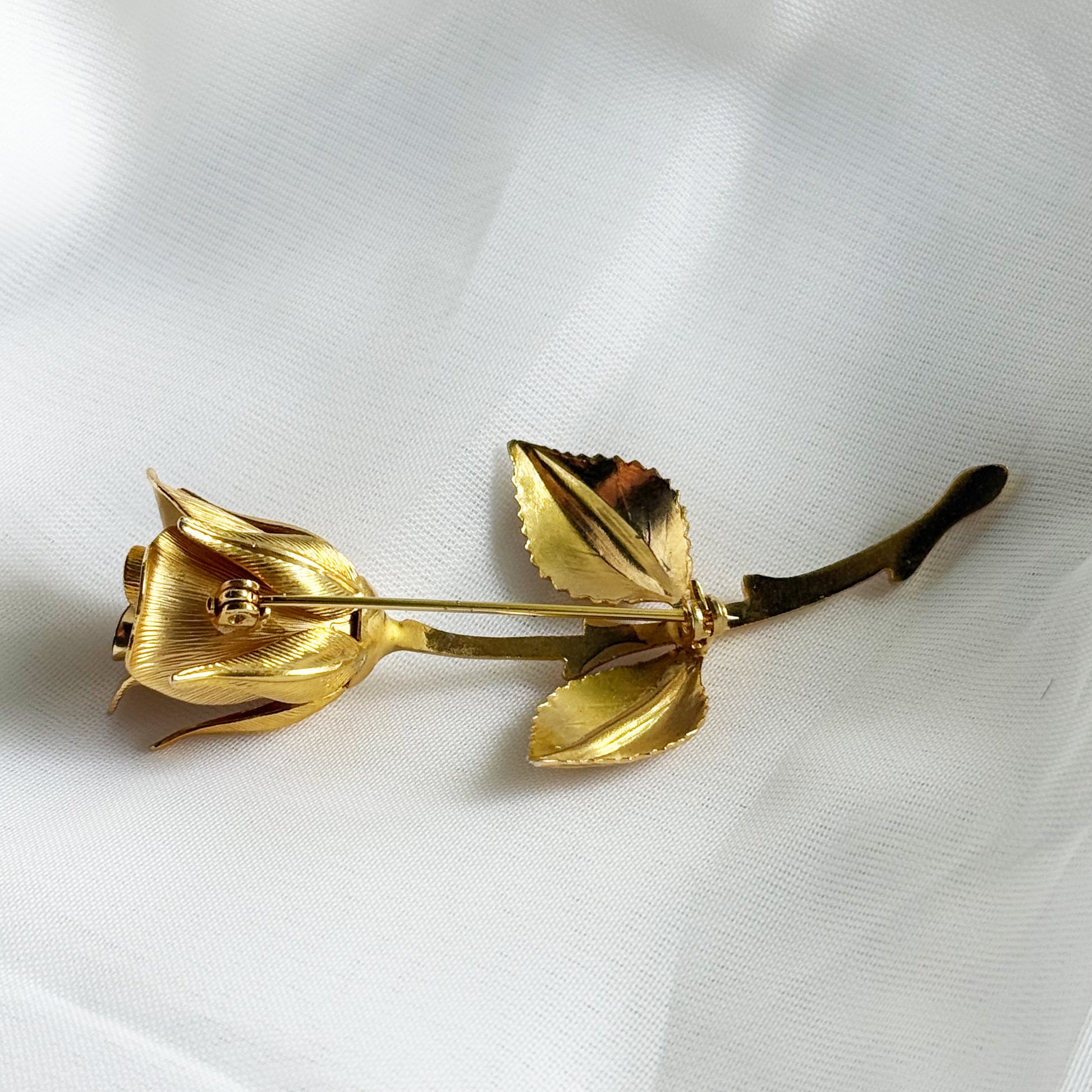 Gold rose-shaped brooch on a white fabric background