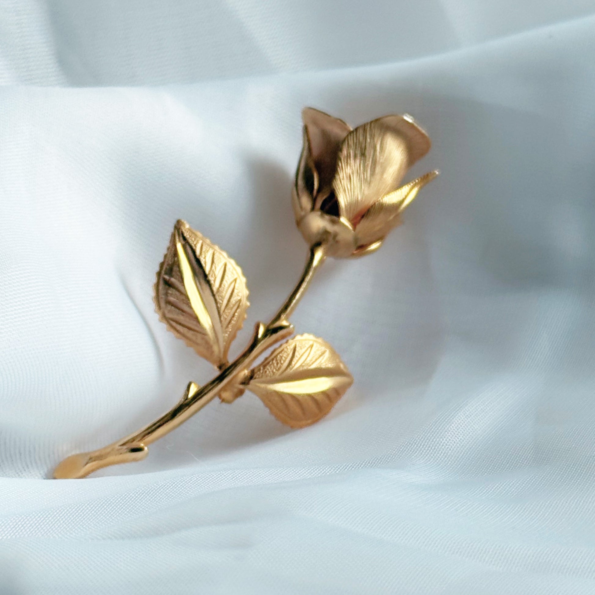 Gold rose-shaped brooch on a white fabric background