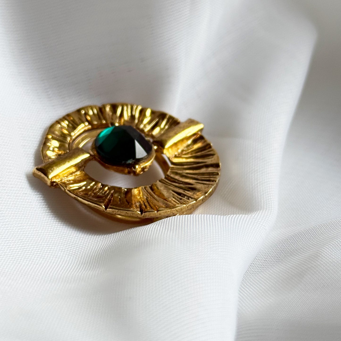 Gold brooch with a central green gemstone on a white fabric background