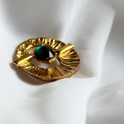 Gold brooch with a central green gemstone on a white fabric background