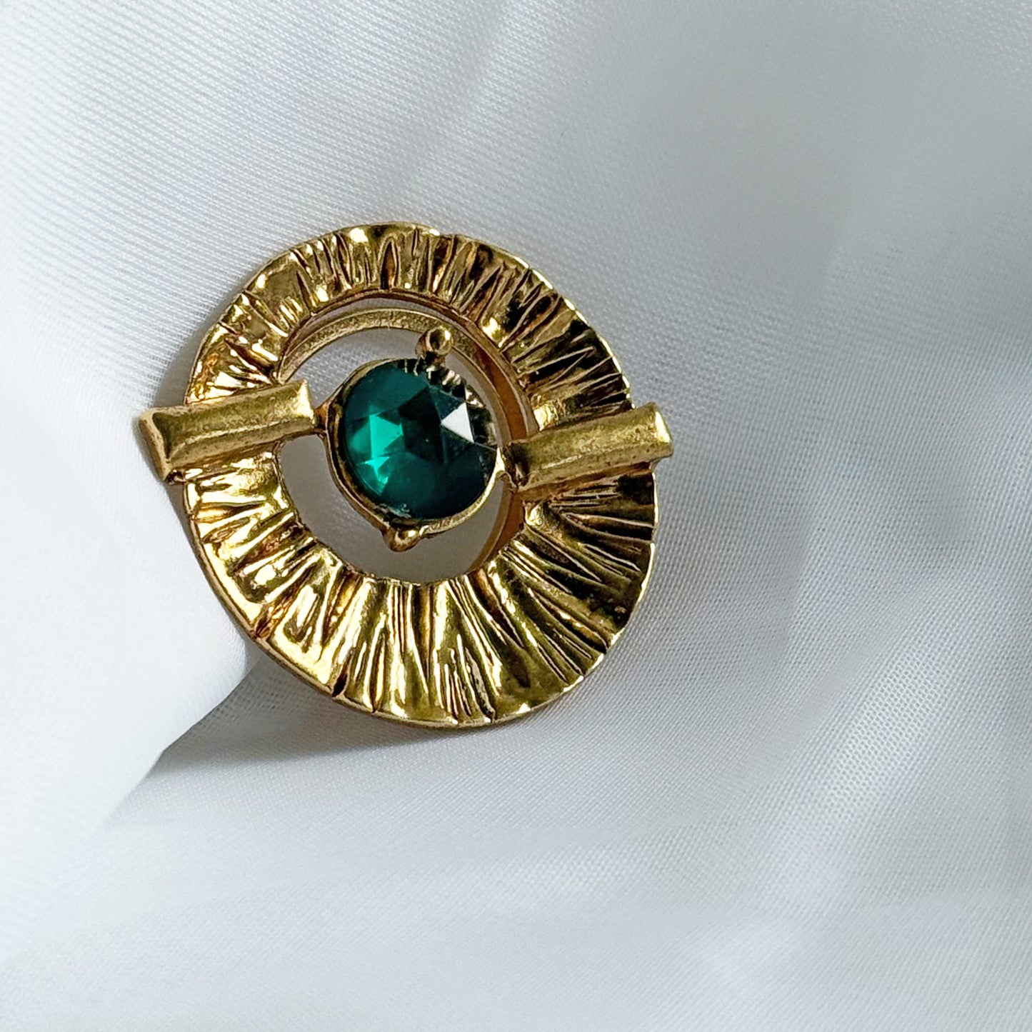 Gold brooch with a green gemstone on a white fabric background