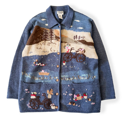Blue jacket with embroidered scenes of a bicycle and nature on a white background