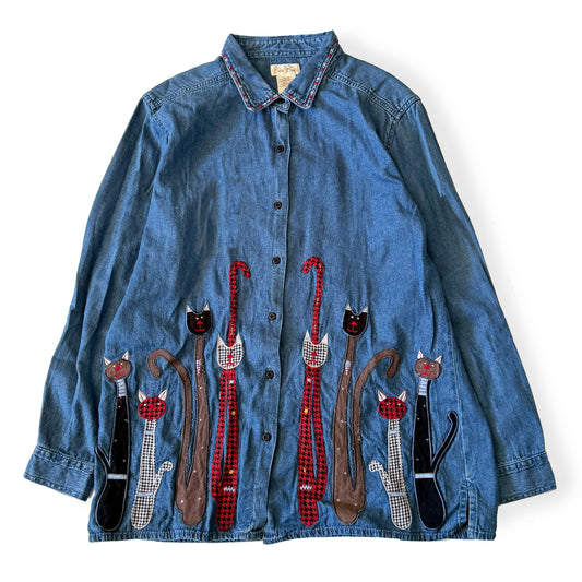 Blue denim shirt with cat appliqués on a white background