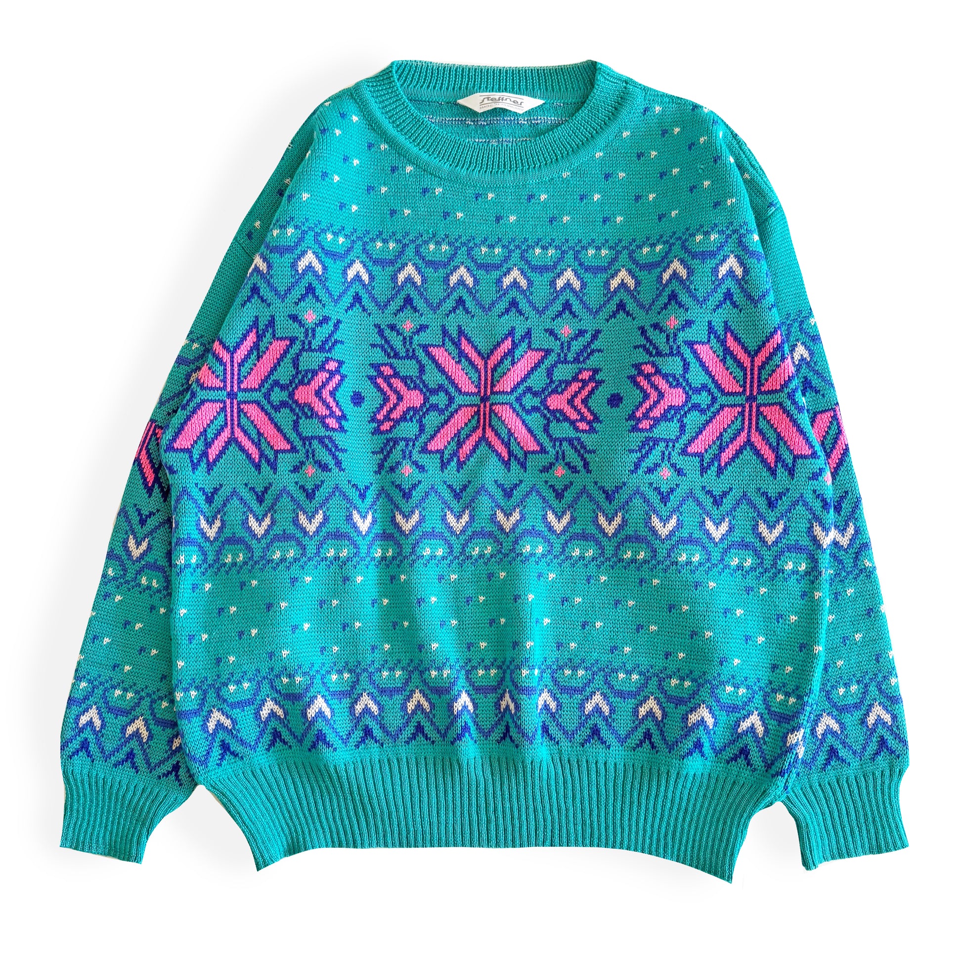 Teal and pink sweater with an aztec / snowflake adjacent style pattern, on a white background. 