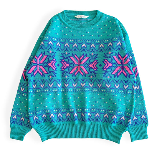 Teal and pink sweater with an aztec / snowflake adjacent style pattern, on a white background. 