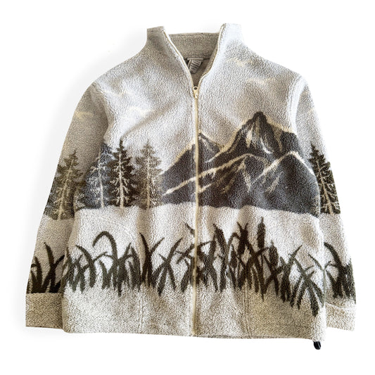 Fleece textured sweater with a mountain marsh forest scene on it, and a zippered close - on a white backdrop. 