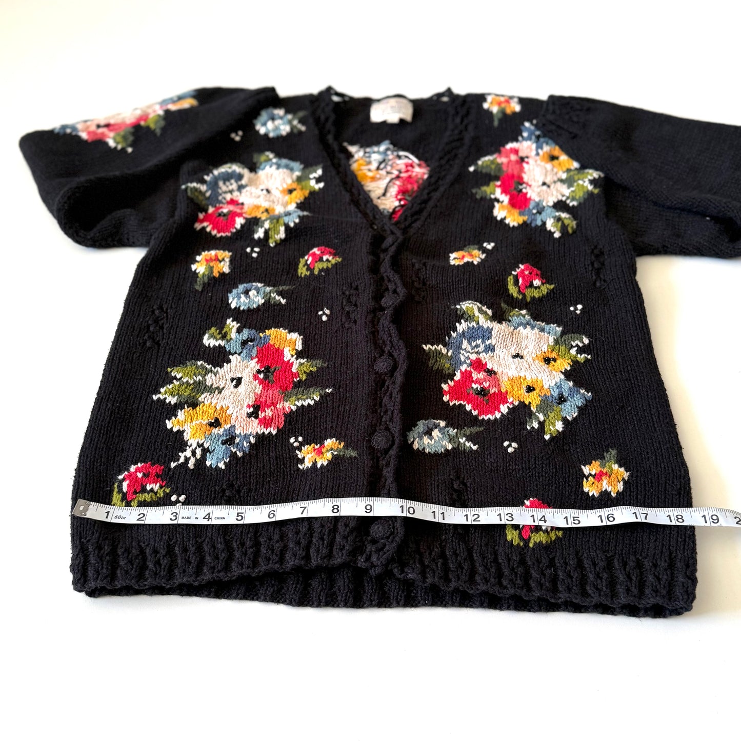 Black cardigan with colorful floral patterns on a white background