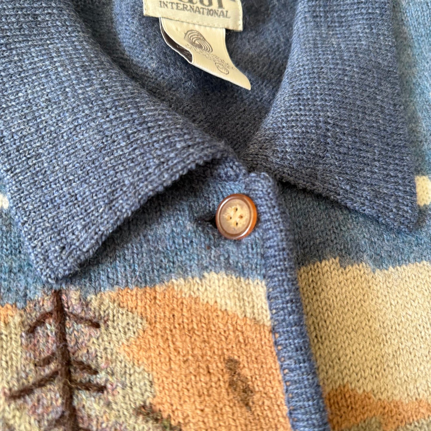 Close-up of a blue patterned jacket with a button and a brand tag.