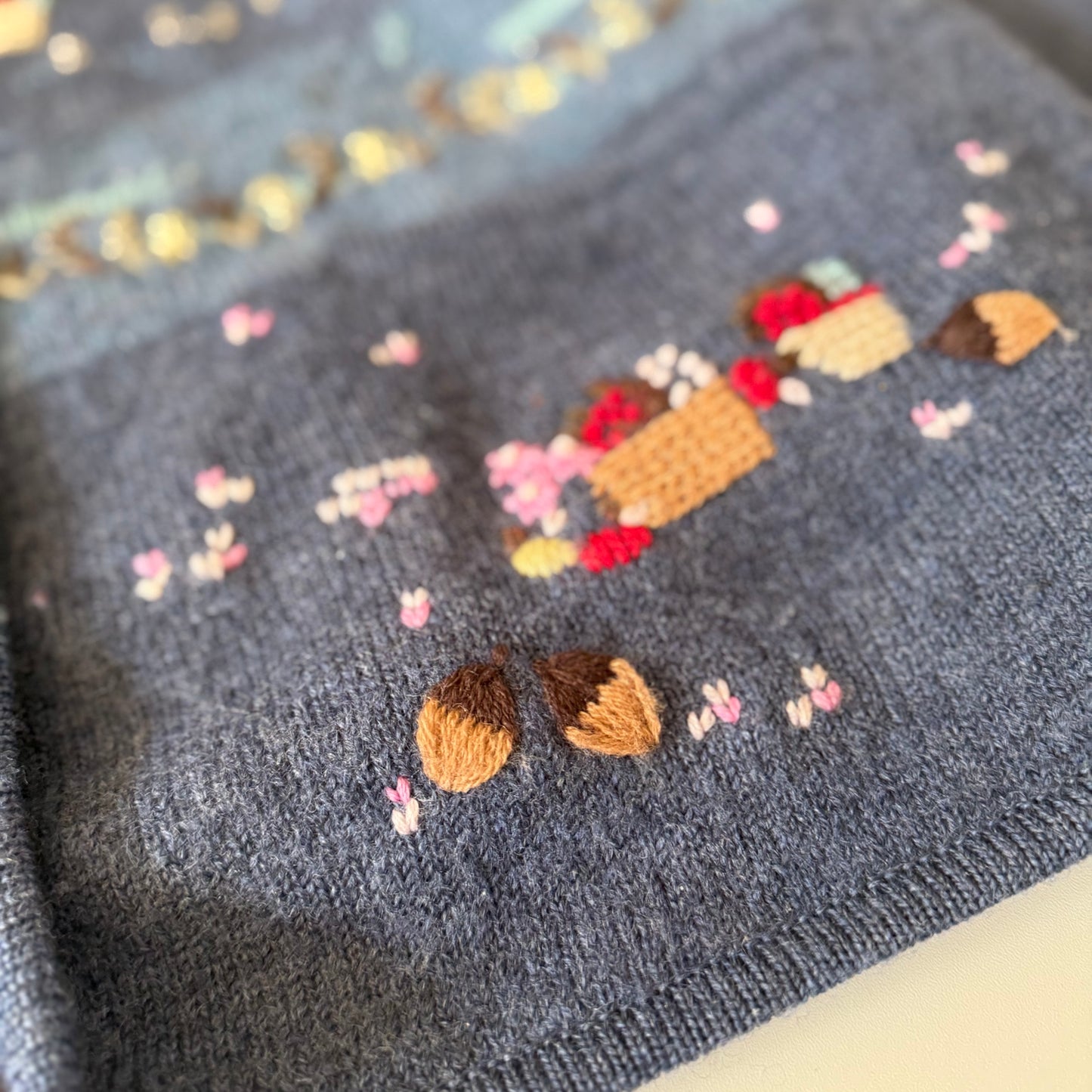 Embroidered design on a gray fabric with acorns and flowers.