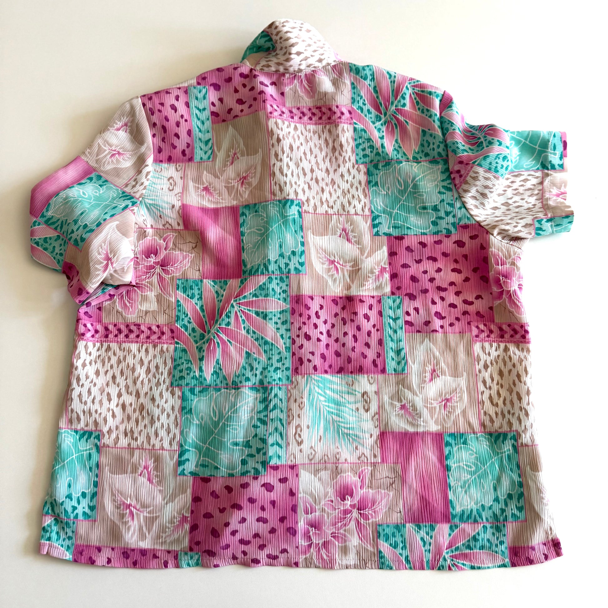 The back side of a button down bright coloured (tan, pink, teal) shirt with tropical and animal print patterns on it - placed on a white background. 