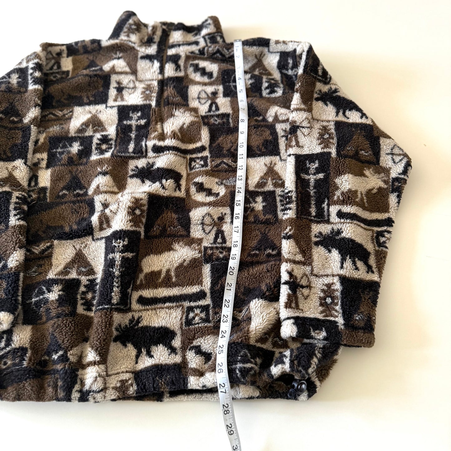 Moose and other camping motif quarter zip fleece on a white background with a measuring tape on it. 