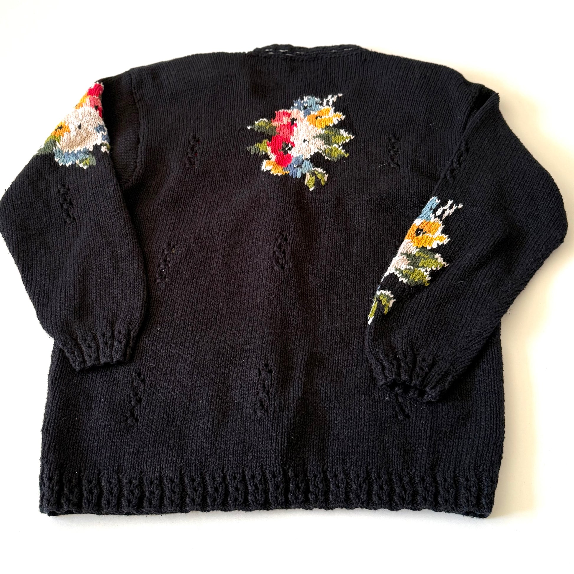 Black knitted sweater with floral patterns on sleeves against a white background