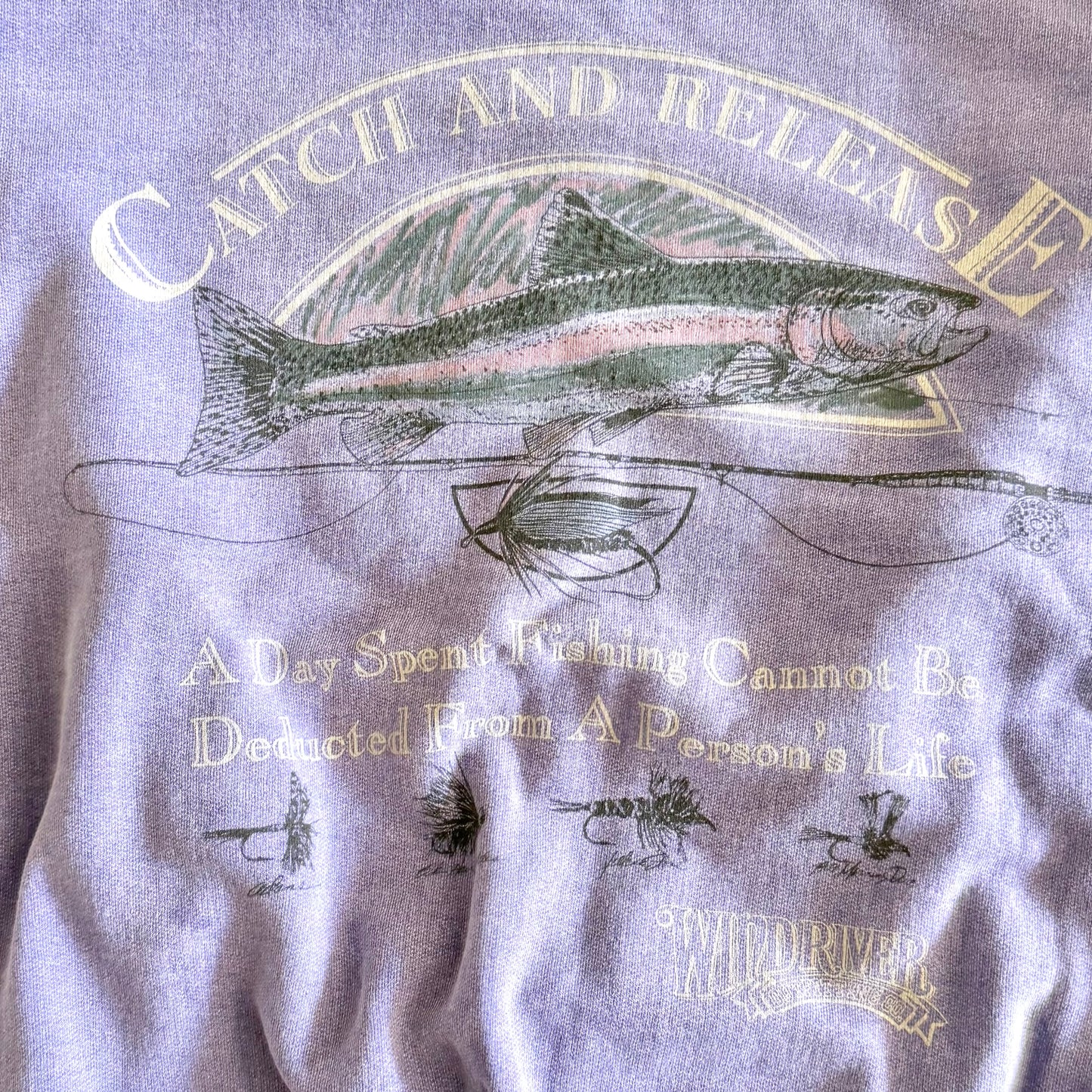 Light purple sweatshirt with fishing theme images and words on the front, close up. 