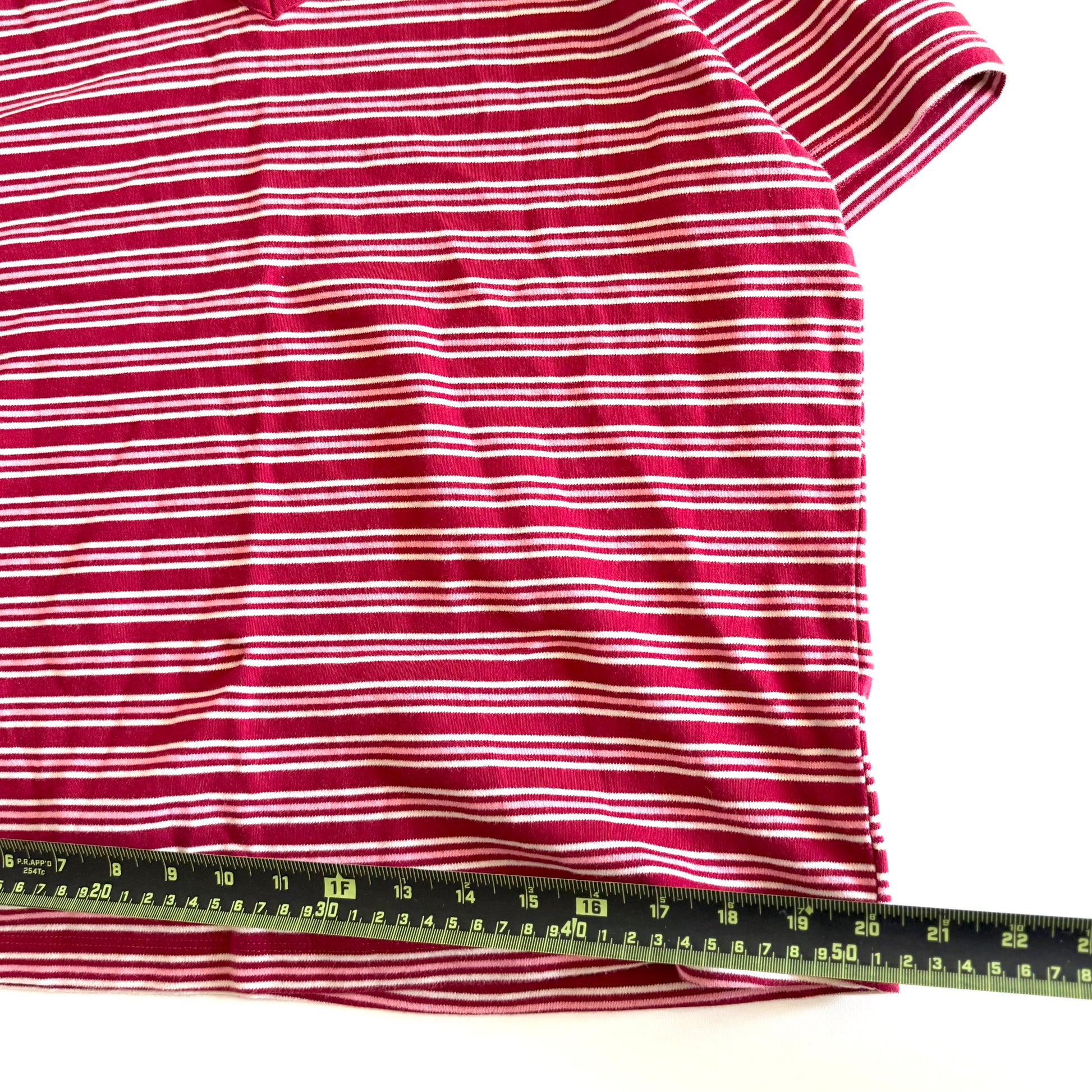 White, pink, and red striped t-shirt with a v-neck collar on a white backdrop - plus a measuring tape laid out on it. 