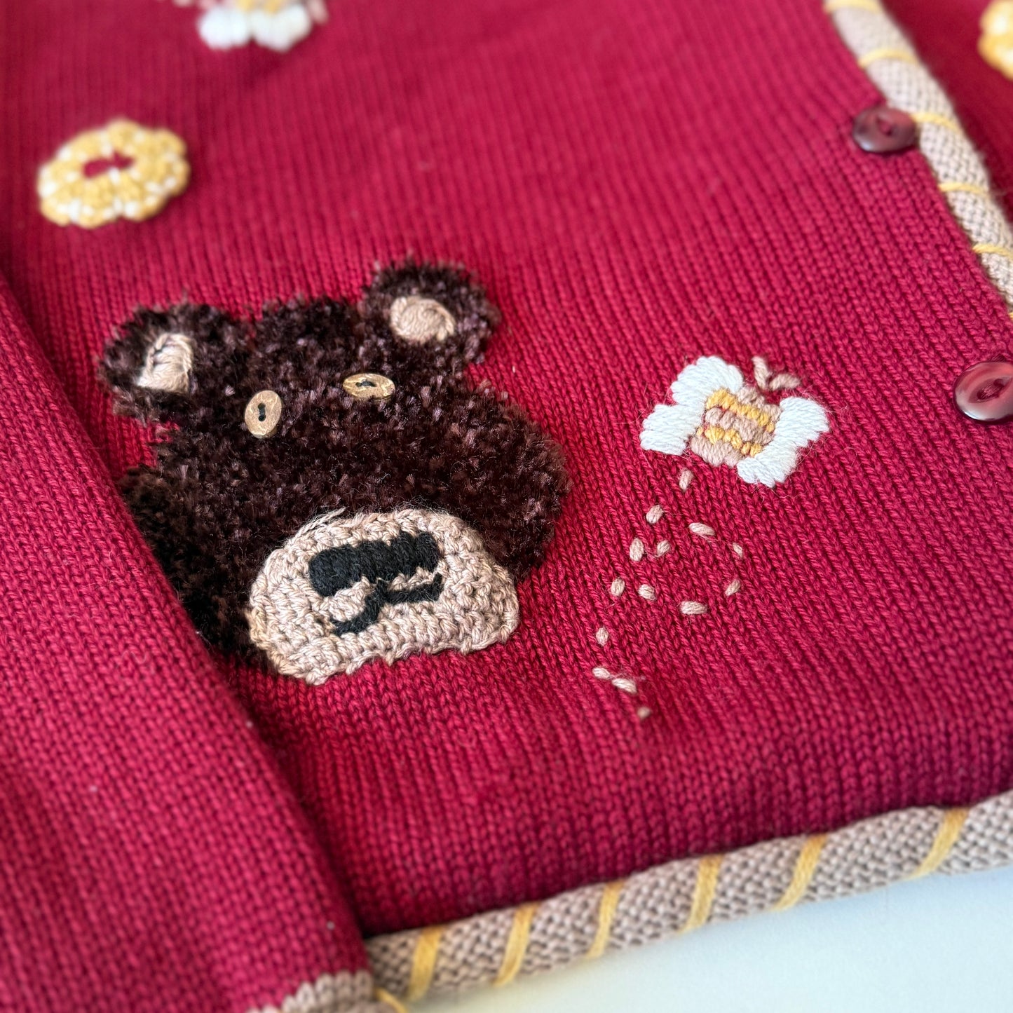 Close-up of a red fabric with a teddy bear patch and floral designs.