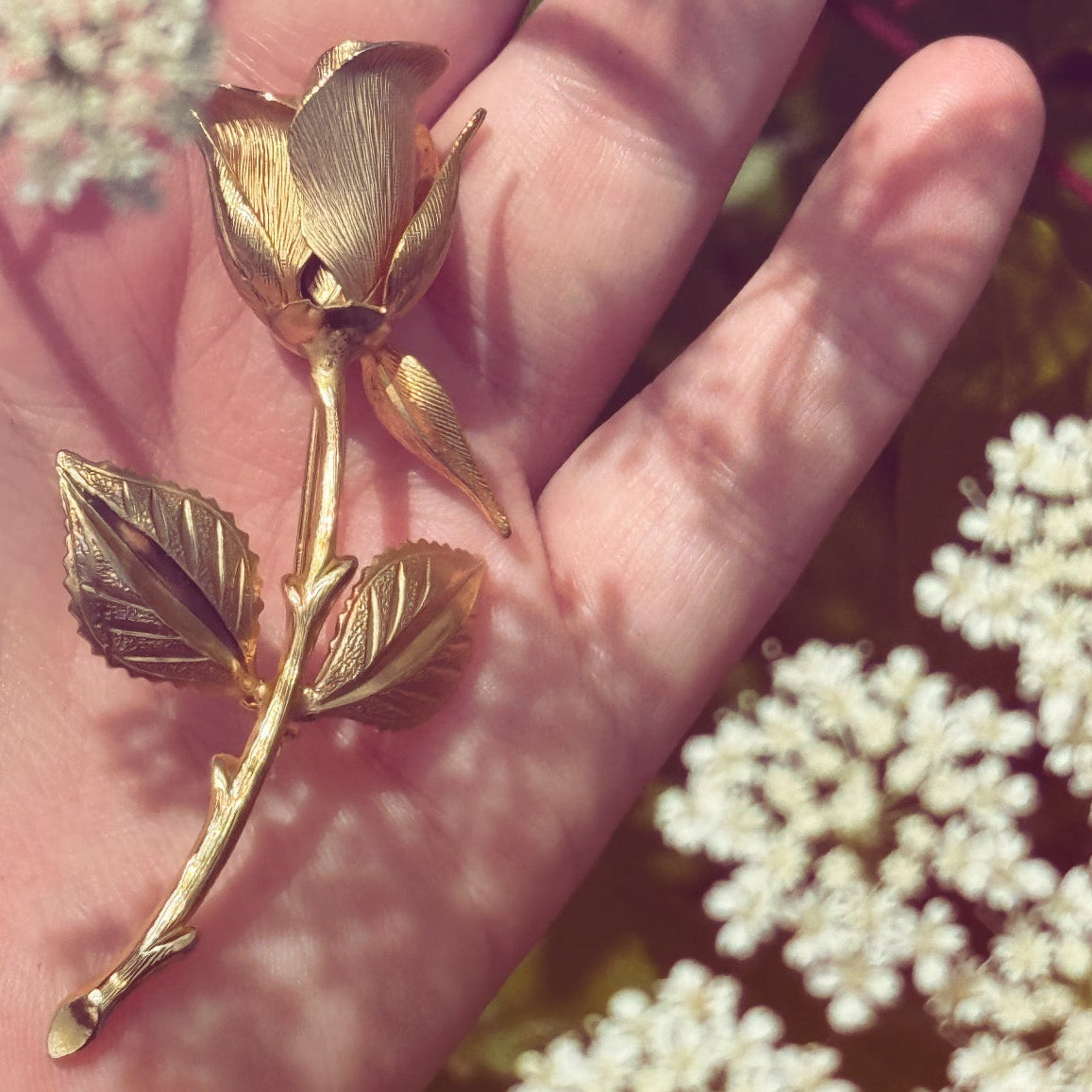 Gold rose brooch held in a hand with a natural background