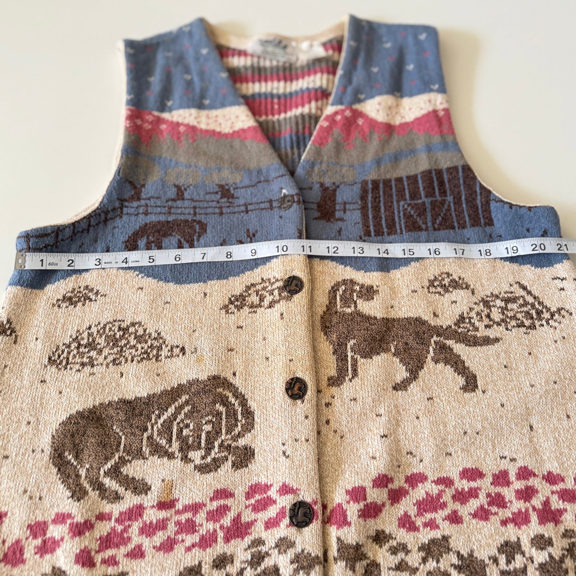 Patterned sweater vest with animals and nature design, partially shown with a measuring tape.