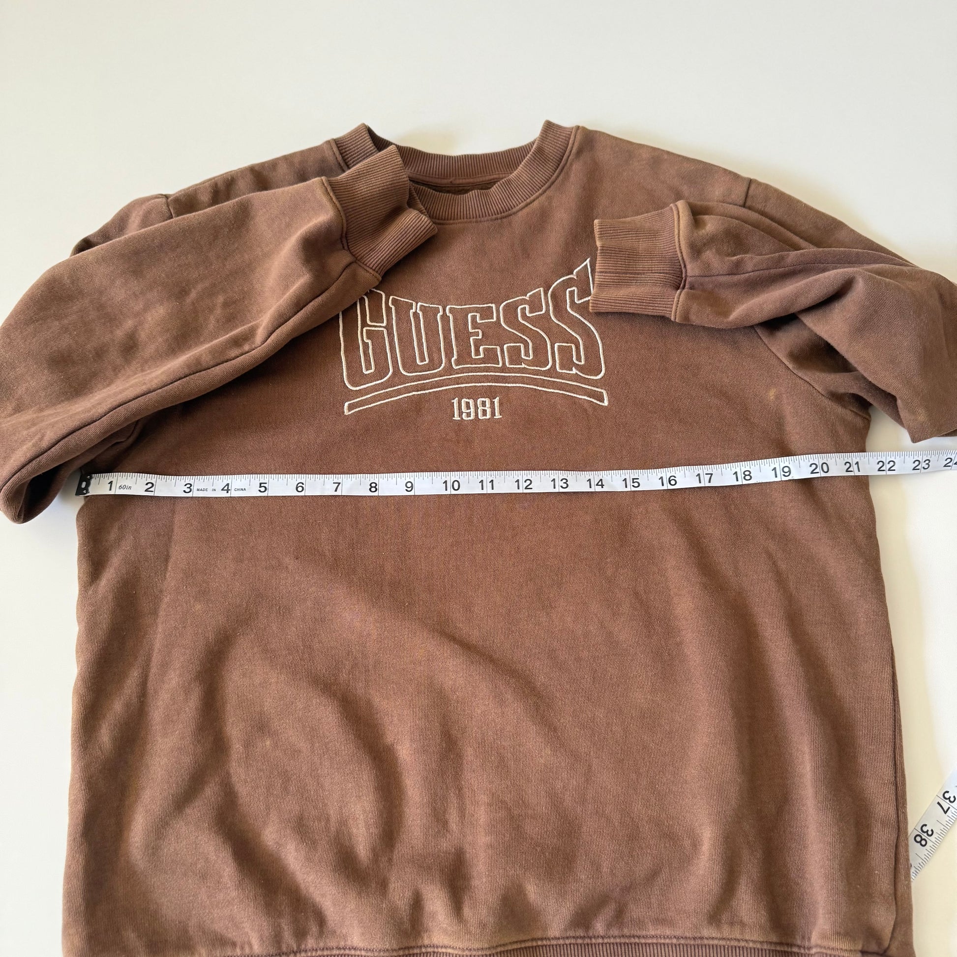 Brown Guess sweatshirt with a measuring tape on a white background