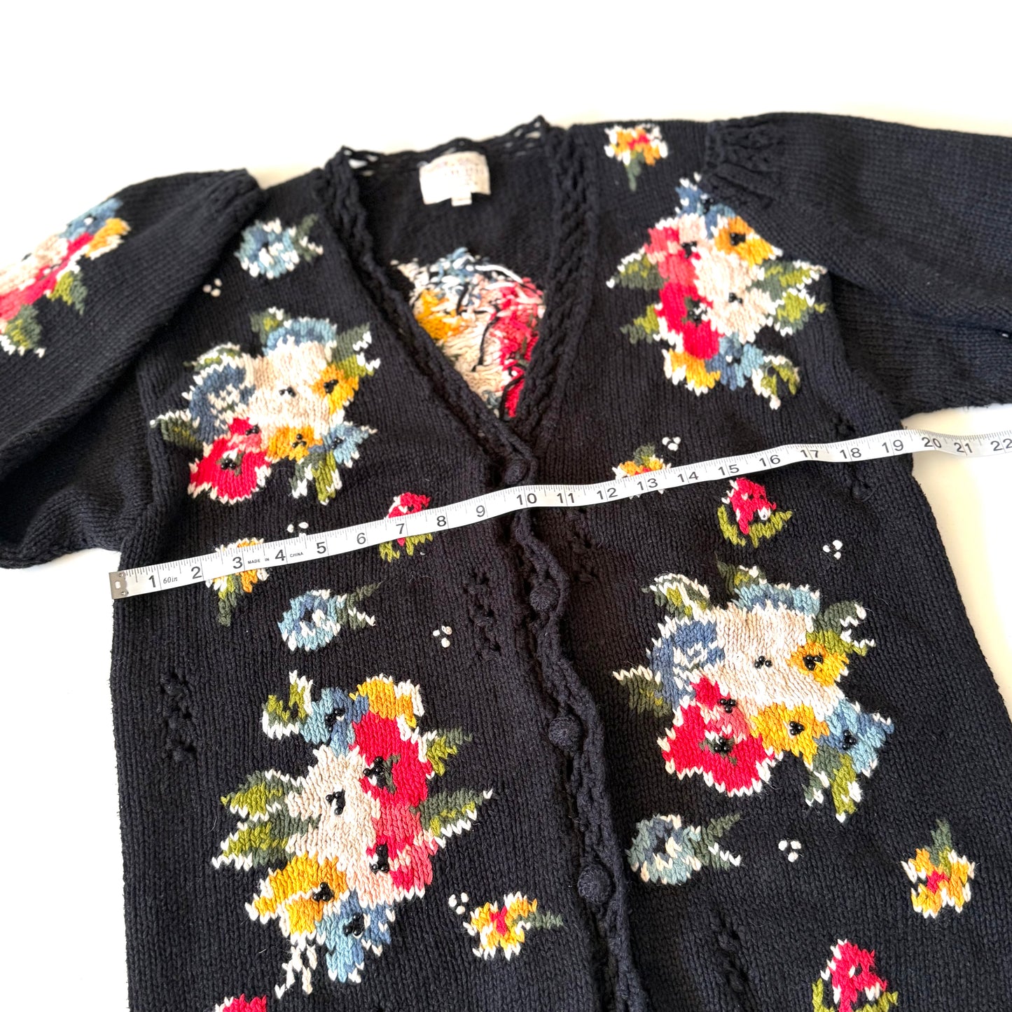 Black cardigan with floral patterns and a measuring tape draped over it on a white background